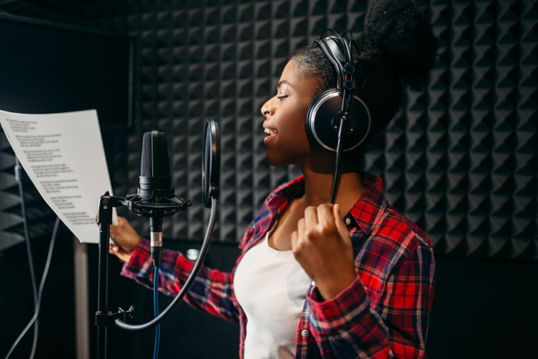 Young woman in headphones songs in audio recording studio. Musician  listens composition, professional music mixing - Fotó, kép
