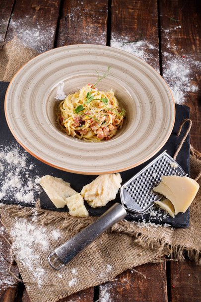 Pasta Carbonara with Parmesan on a white plate. Restaurant food at the wooden table, next to the ingredients for cooking - Φωτογραφία, εικόνα
