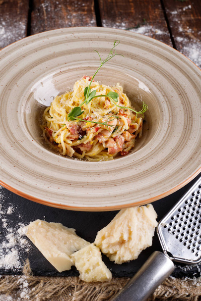 Pasta Carbonara with Parmesan on a white plate. Restaurant food at the wooden table, next to the ingredients for cooking - Foto, afbeelding