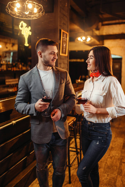 Man and woman drinks red wine at wooden bar counter. Couple leisures in pub, husband and wife relaxing together in a nightclub - Photo, Image