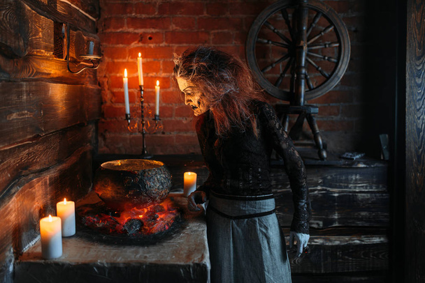 Bruxa assustadora lê feitiço sobre o pote, poderes escuros de bruxaria, sessão espiritual com velas. Mulher previdente chama os espíritos, terrível futuro caixa
 - Foto, Imagem