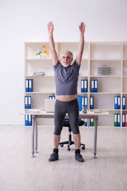 Blanco barbudo viejo empleado haciendo ejercicios en la oficina
  - Foto, imagen