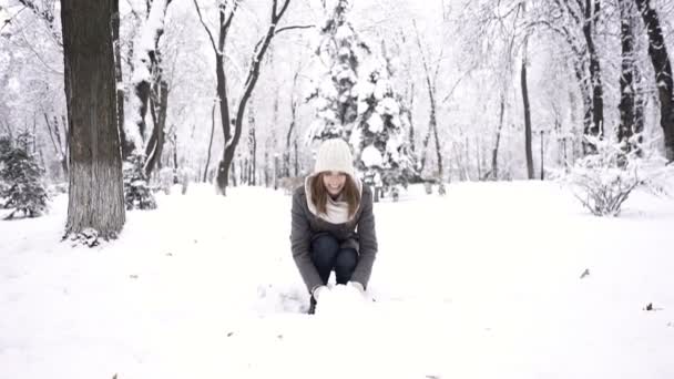 Winter schoonheid. Mooie jonge vrouw gooit sneeuw omhoog in stadspark. Slow motion - Video