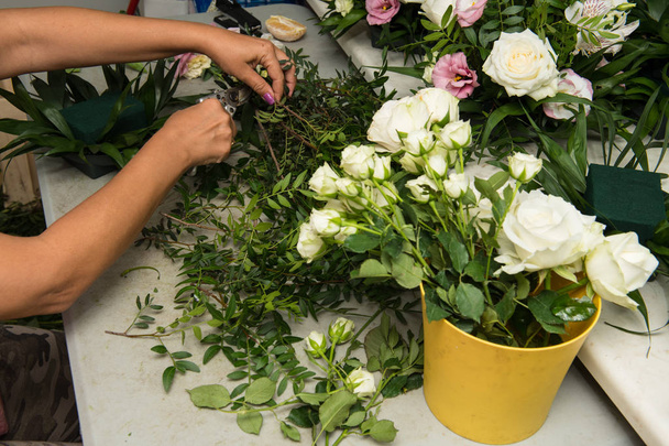 Θηλυκό ανθοκόμος κάνει μια ανθοδέσμη των διαφορετικών λουλουδιών στο τραπέζι εργασίας. - Φωτογραφία, εικόνα