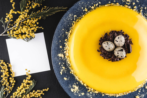 Velikonoční dort se žlutými zrcadlo poleva, čokoládové, jarní květiny, křepelčí vajíčka na tmavém pozadí kamene. Šťastné Velikonoce oslava. Pohled shora, plochá ležel - Fotografie, Obrázek