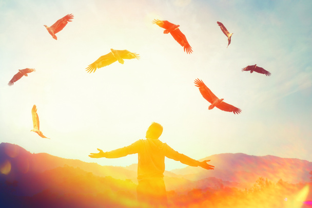 Az ember felemeli a kezét a hegy tetejére, és a naplemente égbolton sas madarak repülnek elvont háttérrel. Másolja tér szabadság utazás kaland és üzleti győzelem koncepció. Vintage hangszűrő hatás színes stílus. - Fotó, kép