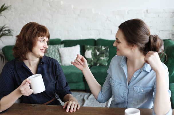 Beautiful mature mother and her adult daughter are drinking coffee  - Photo, Image