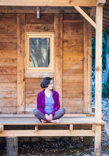 Eine Frau sitzt auf der Veranda eines alten Holzhauses. Barfuß ruht sich das Mädchen an einem warmen Frühlingstag in der Nähe des Hauses aus. - Foto, Bild