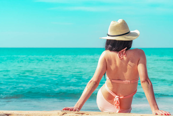 Widok z tyłu szczęśliwy młodej kobiety Azjatki w różowy strój kąpielowy i słomkowy kapelusz zrelaksować się i cieszyć się wakacje w tropikalnym raju plaży o zachodzie słońca. Dziewczyna w wakacje lato moda. Piękna seksowna model. Letnie wibracje. - Zdjęcie, obraz