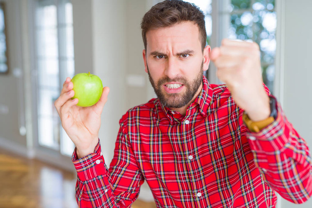 Komea mies syö tuoretta terveellistä vihreää omenaa ärtynyt ja turhautunut huutaa vihaa, hullu ja huutaa kohotettu käsi, viha käsite
 - Valokuva, kuva