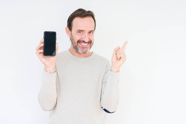Senior man showing smartphone screen over isolated background very happy pointing with hand and finger to the side - 写真・画像