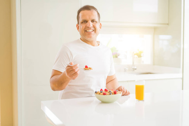 Μέση ηλικία ο άνθρωπος τρώει φράουλες στο σπίτι με ένα χαρούμενο πρόσωπο στέκεται και να χαμογελούν με αυτοπεποίθηση χαμόγελο δείχνει τα δόντια - Φωτογραφία, εικόνα