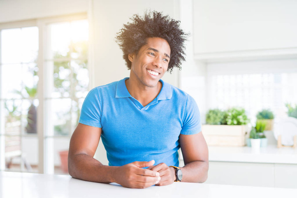 afrikanisch-amerikanischer Mann zu Hause, der mit einem Lächeln im Gesicht und natürlichem Gesichtsausdruck zur Seite schaut. Lachen selbstbewusst. - Foto, Bild