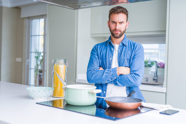 Handsome man cooking italian spaghetti pasta at the kitchen skeptic and nervous, disapproving expression on face with crossed arms. Negative person. - Photo, Image