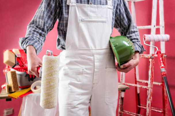Fiatal fehér házfestő munkás fehér munkaruhában, a kezével tartja a hengert. Építőipar. Munkabiztonság.  - Fotó, kép