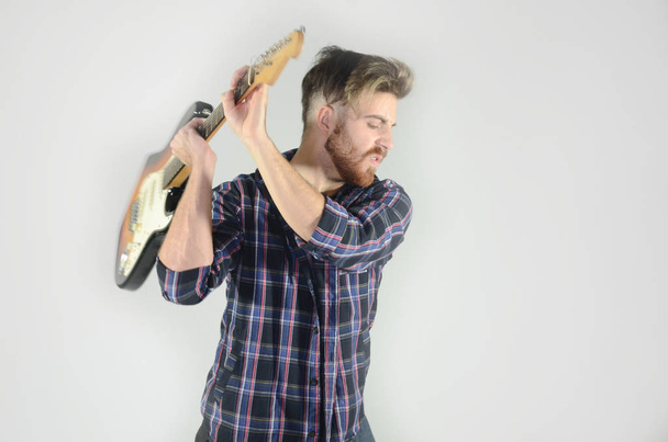 Young man wearing casual breaking an electric guitar on isolated white background - Photo, image