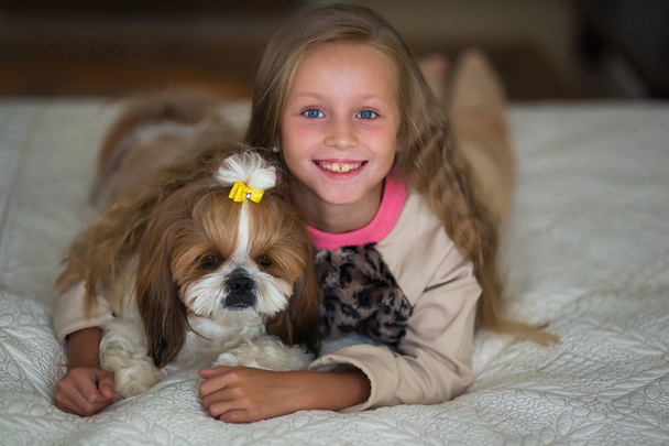 Cute girl with long hair is lying on the sofa with a dog at home. - Zdjęcie, obraz