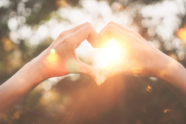 Female hands heart shape on nature bokeh sun light flare and blur leaf abstract background. Copy space of happy love and freedom concept. Vintage tone filter color style. - Photo, Image