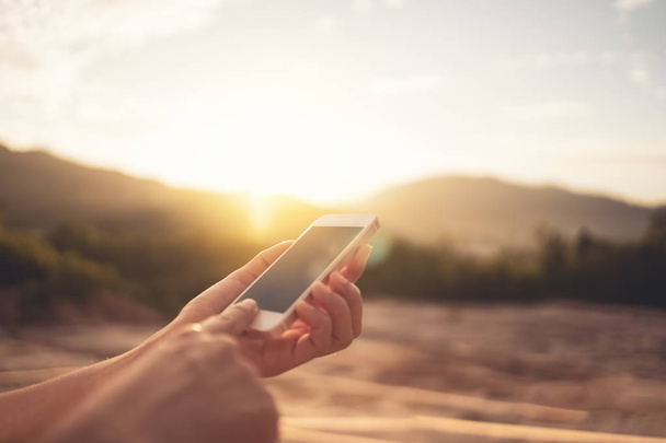 Donna mano utilizzando smart phone in cima alla montagna con cielo tramonto sfondo astratto
. - Foto, immagini