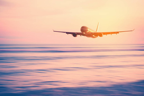 Avión volando sobre la borrosa playa tropical con suave ola y puesta de sol cielo fondo abstracto
. - Foto, imagen