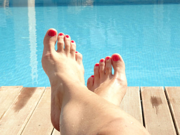 Pieds féminins avec vernis à ongles rouge devant une piscine
 - Photo, image