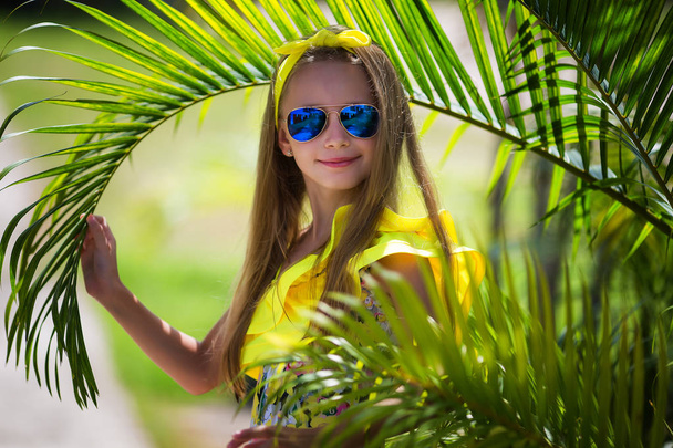 Beautiful girl with long hair in a yellow swimsuit and multi-colored sunglasses on the background of palm trees - Foto, immagini