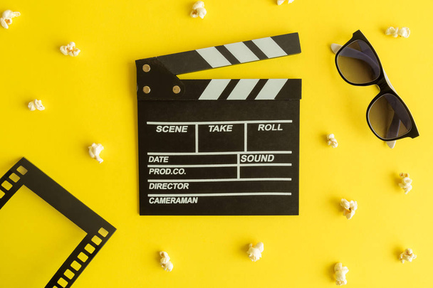 Cinema and movie making background. Clapperboard with 3d glasses, frame in form of film strip and popcorn isolated on yellow background minimal creative concept. - Foto, Imagen