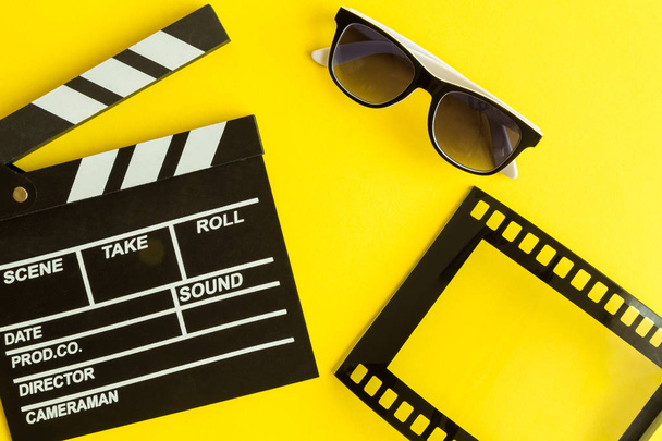 Flat lay of clapper board and glasses with film strip frame isolated on yellow. - Foto, Imagen