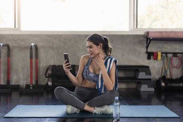χρησιμοποιώντας το smartphone μετά την άσκηση σε γυμναστήριο της Ασίας γυναίκες.  - Φωτογραφία, εικόνα