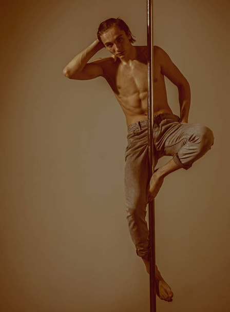 Young strong man pole dancing on grey background. - Foto, imagen