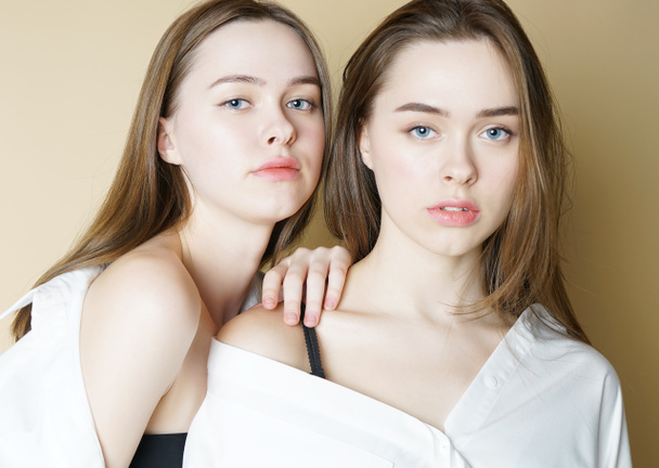 Moda belleza modelos dos hermanas gemelas hermosas chicas desnudas mirando a la cámara aislada sobre fondo beige
 - Foto, Imagen