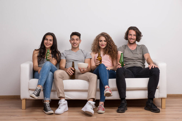 Portrait of young group of friends sitting on a sofa in a studio, holding bottles. - Foto, immagini