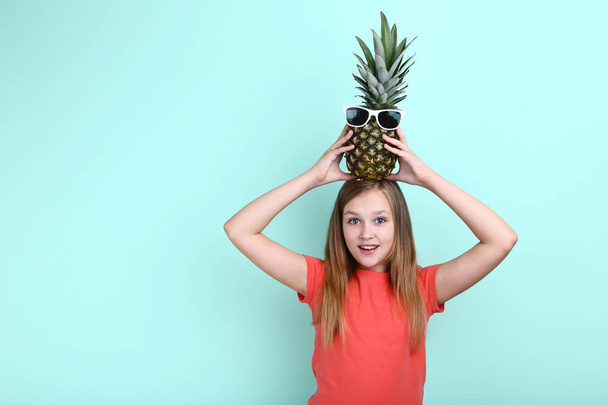 Cute young girl with pineapple in sunglasses on mint background - Foto, afbeelding