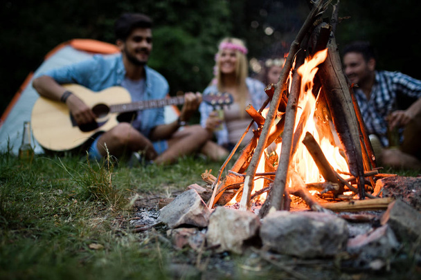 Happy friends playing music and enjoying bonfire in nature - Photo, Image
