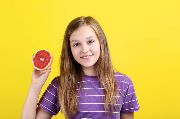 Cute young girl with grapefruit on yellow background - 写真・画像