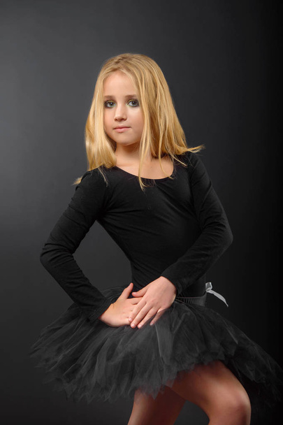 Cute little ballerina with long hair in a black tutu and pointe posing on a black background - Foto, imagen