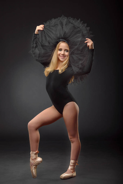 Cute little ballerina with long hair in a black tutu and pointe posing on a black background - Photo, image