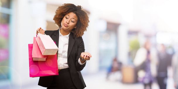 Fiatal fekete nő gazdaság bevásárló táskák, zavaros, és a kétes - Fotó, kép