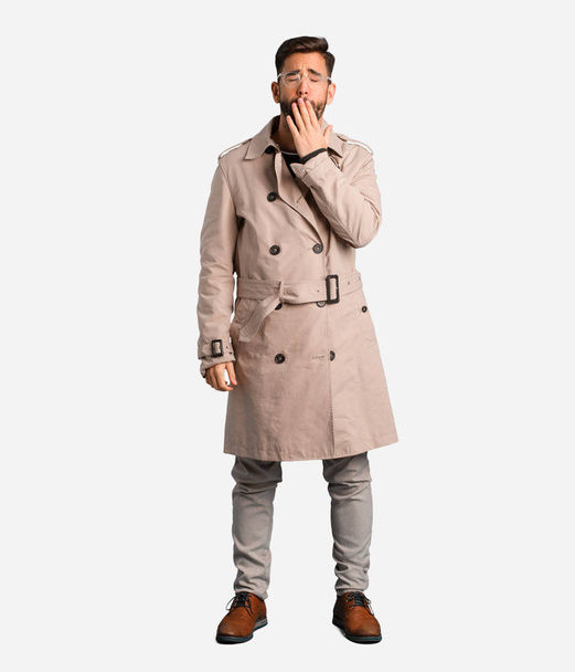 Young man wearing trench coat tired and very sleepy - Photo, Image