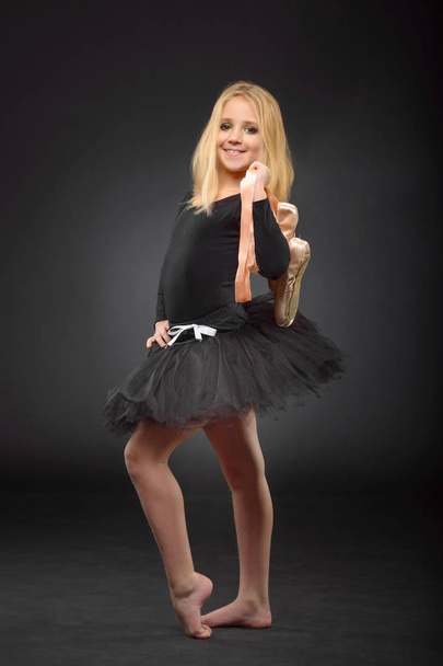 Cute little ballerina with long hair in a black tutu and pointe posing on a black background - Foto, afbeelding