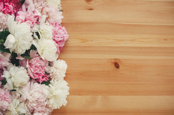 Stijlvolle roze en witte pioenrozen grens op houten tafel, plat lag  - Foto, afbeelding