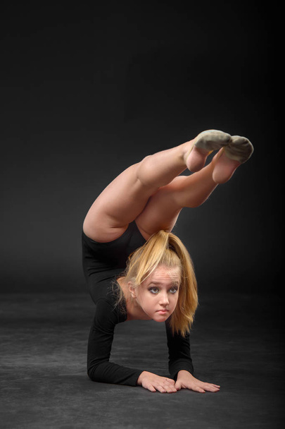 Young beautiful white caucasian girl gymnast with long hair doing gymnastic exercise on black background. - Φωτογραφία, εικόνα