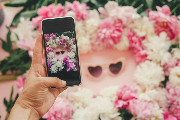 Рука тримає телефон і фотографує сонцезахисне скло у формі рожевого серця
 - Фото, зображення