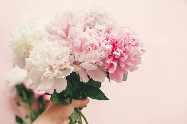 Hand met stijlvolle roze en witte pioenrozen boeket op roze pape - Foto, afbeelding