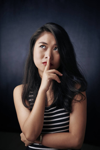 Портрет смішної молодої жінки з пальцем на губах, що мріє про щось на чорному тлі
 - Фото, зображення