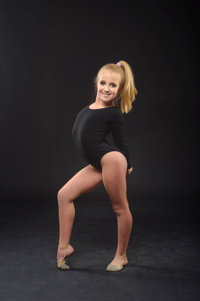 Young beautiful white caucasian girl gymnast with long hair doing gymnastic exercise on black background. - Photo, image