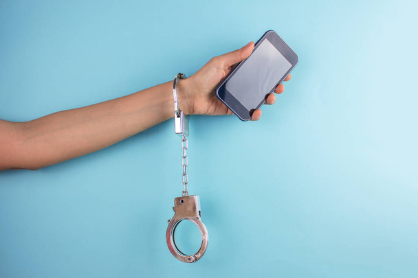 обрезанный снимок женской руки со смартфоном в наручниках
 - Фото, изображение