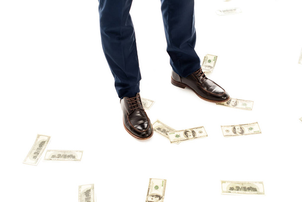 Teilansicht eines Geschäftsmannes mit Geld unter den Füßen, isoliert auf weißem Grund - Foto, Bild