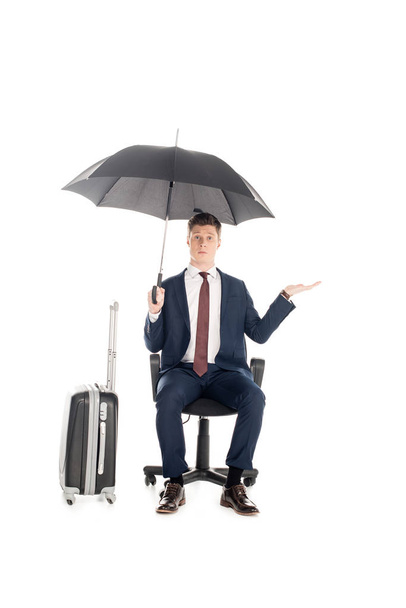 businessman sitting on chair with umbrella and baggage for business trip, isolated on white  - Fotó, kép