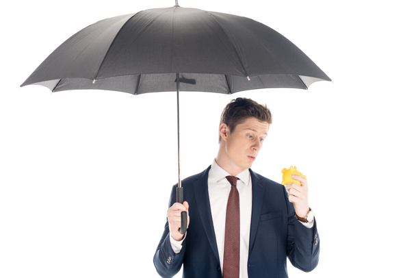 young businessman with umbrella looking at little piggy bank isolated on white  - Fotografie, Obrázek